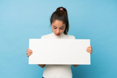 Genç esmer kız izole edilmiş mavi arka planda boş beyaz bir levha tutuyor.