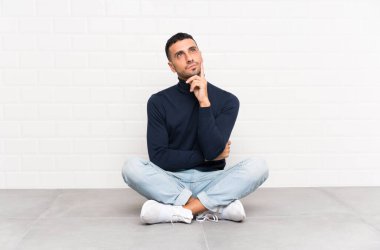 Genç yakışıklı bir adam yerde oturmuş bir fikir düşünüyor.