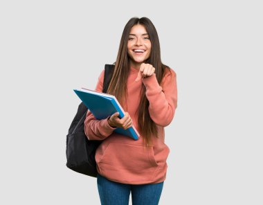 Elinde not defterleri olan genç bir bayan, gri arka plan üzerinde şaşırmış ve ön tarafı işaret ediyor.