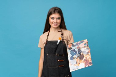 Bir palet tutan, soyutlanmış mavi arka planı olan genç bir kadın.