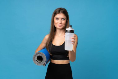 Genç bir kadın, izole edilmiş arka planda, spor su şişesi ve paspasla.
