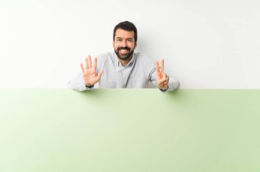 Sakallı genç yakışıklı adam elinde kocaman yeşil boş bir pankart yedi parmaklı sayıyor.