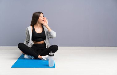 Genç spor kadın ağzı tamamen açık bağırarak mat ile katta oturan