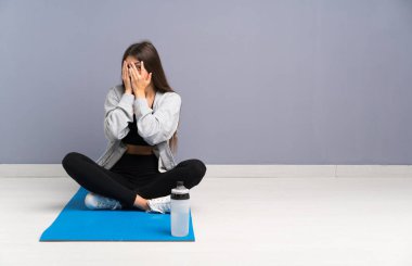 Genç sporcu kadın yerde oturuyor, gözleri örtüyor ve parmaklarından bakıyor.