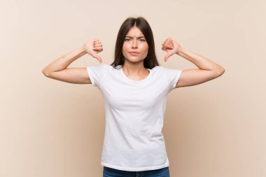 İzole edilmiş arka planda güzel bir genç kız baş parmağını aşağı gösteriyor.