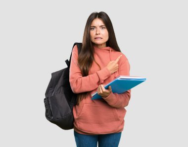 Elinde not defterleri tutan genç bir bayan. Korkmuş ve gri arka plan üzerinde bir kenarı işaret ediyor.