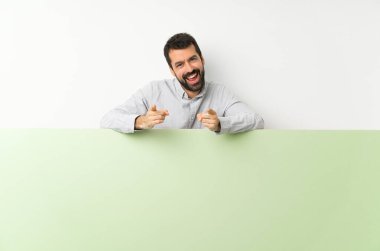 Sakallı, kocaman boş bir levha tutan genç yakışıklı adam gülümserken parmağını sana gösteriyor.