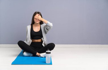 Genç sporcu kadın yerde oturuyor. Paspasla gözleri örtülmüş.