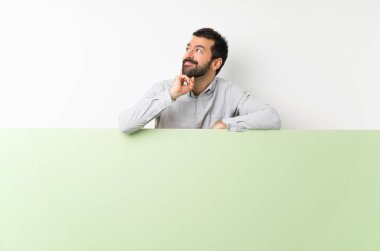 Sakallı, kocaman yeşil bir pankart tutan yakışıklı genç adam yukarı bakarken bir fikir düşünüyor.