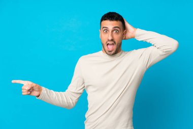 Soyutlanmış mavi arka planı olan genç adam şaşırdı ve parmağını yana uzattı.