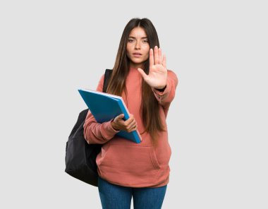 Elinde not defterleri olan genç bir bayan izole edilmiş gri arka planda dur hareketi yapıyor.