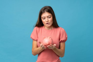 Soyutlanmış mavi arka planı olan genç bir kadın büyük bir kumbara tutuyor.