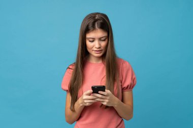 İzole edilmiş mavi arka plan üzerinde genç bir kadın cep telefonuyla bir mesaj ya da e-posta gönderiyor