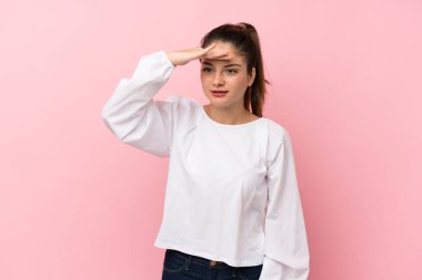 Soyutlanmış pembe arka planda genç esmer kız uzaklarda bir şeye bakmak için el ele bakıyor.