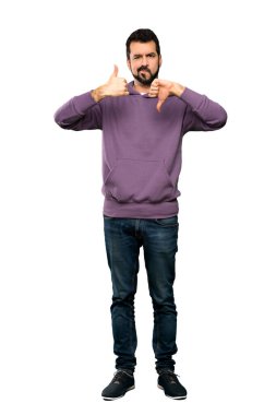 Sweatshirt 'lü yakışıklı adamın iyi-kötü işareti yaptığı uzun bir çekim. İzole edilmiş beyaz arkaplan arasında kararsızlık