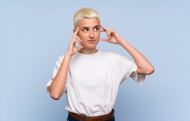 Teenager girl with white short hair over blue wall having doubts and thinking