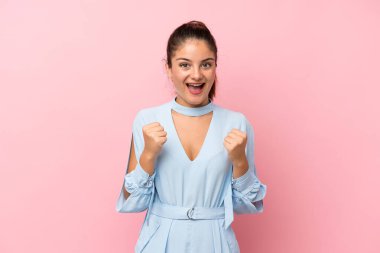 Genç esmer kız izole edilmiş pembe arka planda zaferi kutluyor.