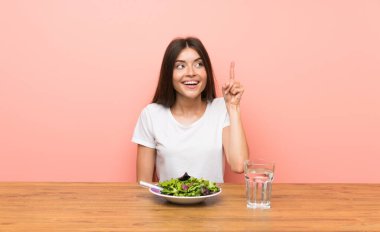 Elinde salata olan genç bir kadın parmağını kaldırarak çözümü anlamaya çalışıyor.