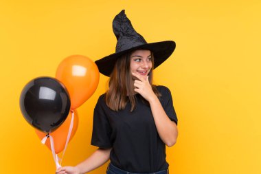 Cadılar bayramı partileri için elinde siyah ve turuncu balonlar tutan genç cadı.