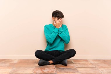 Genç yakışıklı adam gözleri kaplayan ve parmaklardan bakarak katta oturan