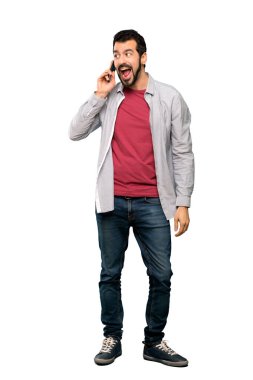 Sakallı, yakışıklı bir adamın izole edilmiş beyaz arka planda cep telefonuyla sohbet ederken tam boy görüntüsü.