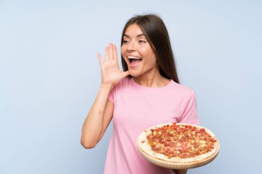 Güzel genç bir kız, izole edilmiş mavi duvarın üzerinde pizza tutuyor ve ağzı açık bağırıyor.