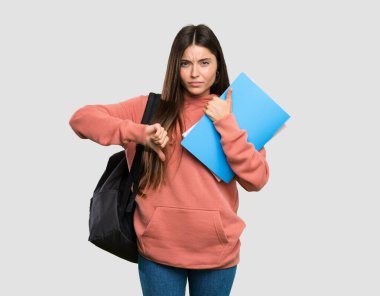 Elinde not defterleri olan genç bir bayan iyi-kötü tabela yapıyor. İzole edilmiş gri arkaplan arasında kararsız