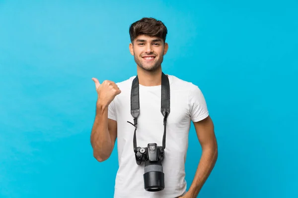 年轻英俊的男子用专业相机和指向侧边的孤立的蓝色背景 — 图库照片