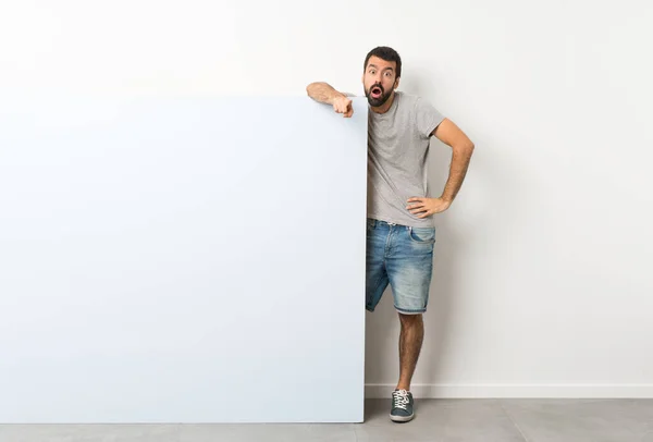 Young Handsome Man Beard Holding Big Blue Empty Placard Surprised — Stock Photo, Image