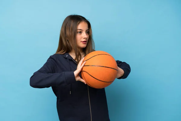 一个年轻的黑发女孩带着篮球运动越过了孤立的蓝色背景 — 图库照片