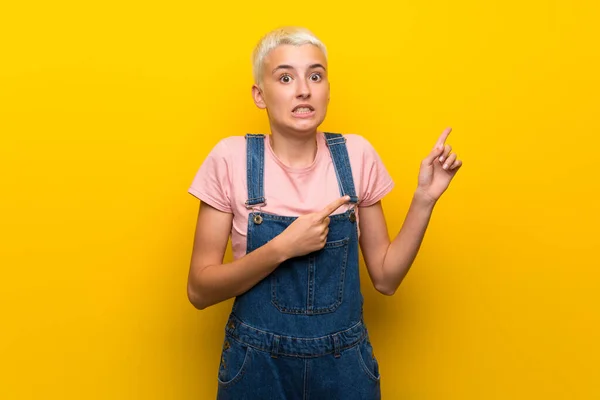 Menina Adolescente Com Macacão Fundo Amarelo Assustado Apontando Para Lado — Fotografia de Stock