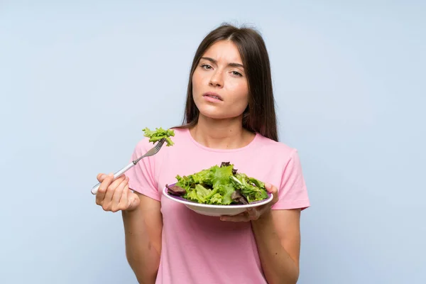 Young woman with salad over isolated blue background