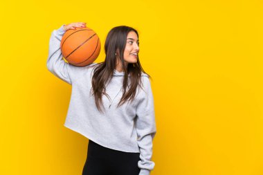 İzole sarı arka plan üzerinde basketbol oynayan genç kadın