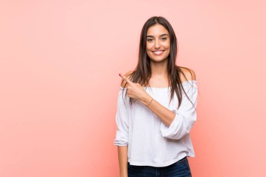 Soyutlanmış pembe arka planı olan genç bir kadın bir ürünü sunmak için kenarı işaret ediyor.