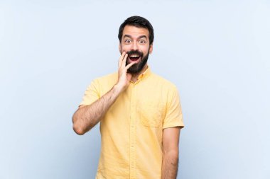 Sakallı genç bir adam mavi arka planda, şaşırmış ve şok olmuş bir yüz ifadesi var.