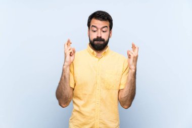 Mavi arka planda sakallı genç bir adam parmaklarını çapraz yapıp en iyisini diliyor.