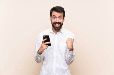 Sakallı genç adam, kazanan pozisyonda zaferi kutlayan bir cep telefonu tutuyor.