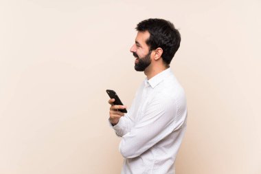 Sakallı genç adam yan pozisyonda cep telefonu tutuyor.