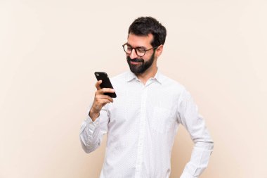 Sakallı genç adam cep telefonunu tutuyor ve gülümsüyor.