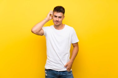 Soyutlanmış sarı arka planı olan yakışıklı bir genç. Şüpheleri var.