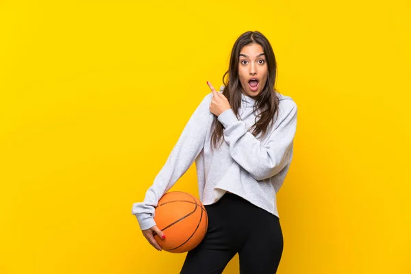 Młoda Kobieta Gra Koszykówkę Odizolowanym Żółtym Tle Zaskoczony Wskazując Bok — Zdjęcie stockowe