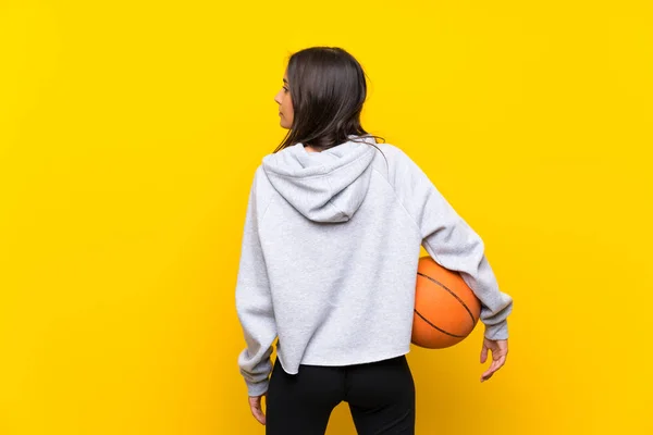 Wanita muda bermain basket melalui latar belakang kuning yang terisolasi — Stok Foto