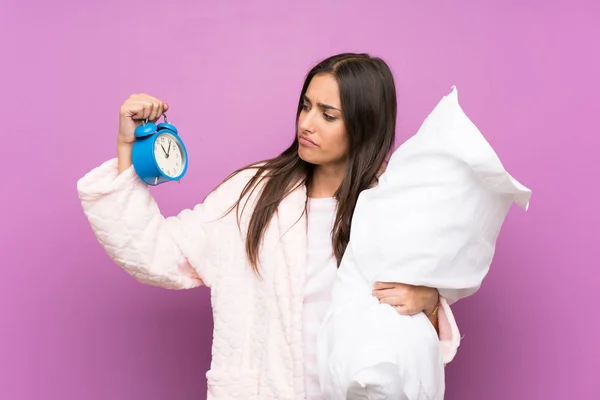 Молодая женщина в пижаме и халате на изолированном фиолетовом фоне держа винтажные часы — стоковое фото