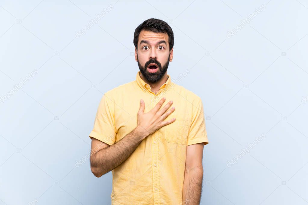 Young man with beard over isolated blue background surprised and shocked while looking right