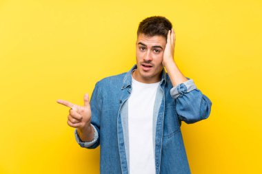 Genç, yakışıklı, izole edilmiş sarı arka planı olan, şaşırmış ve işaret eden bir adam.
