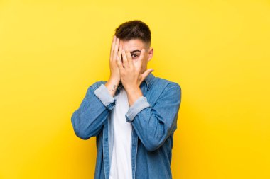 Gözleri kaplayan izole sarı arka plan üzerinde genç yakışıklı adam ve parmaklardan bakarak