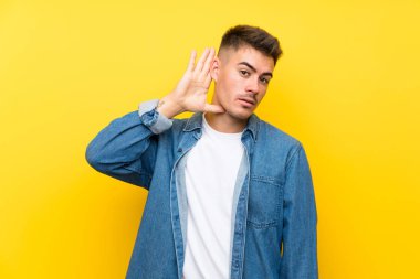 Izole sarı arka plan üzerinde genç yakışıklı adam bir şey dinlerken