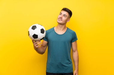 Yakışıklı genç futbolcu, izole edilmiş sarı arka planda gülümserken yukarı bakıyor.