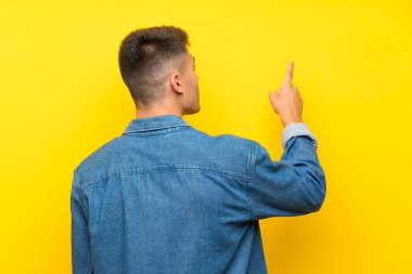 Soyutlanmış sarı arka planda genç yakışıklı adam işaret parmağıyla işaret ediyor.