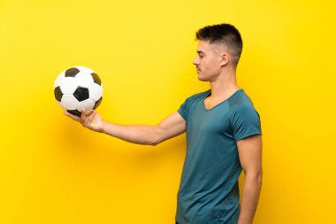 Yakışıklı genç futbolcu mutlu bir ifadeyle izole edilmiş sarı arka planda.